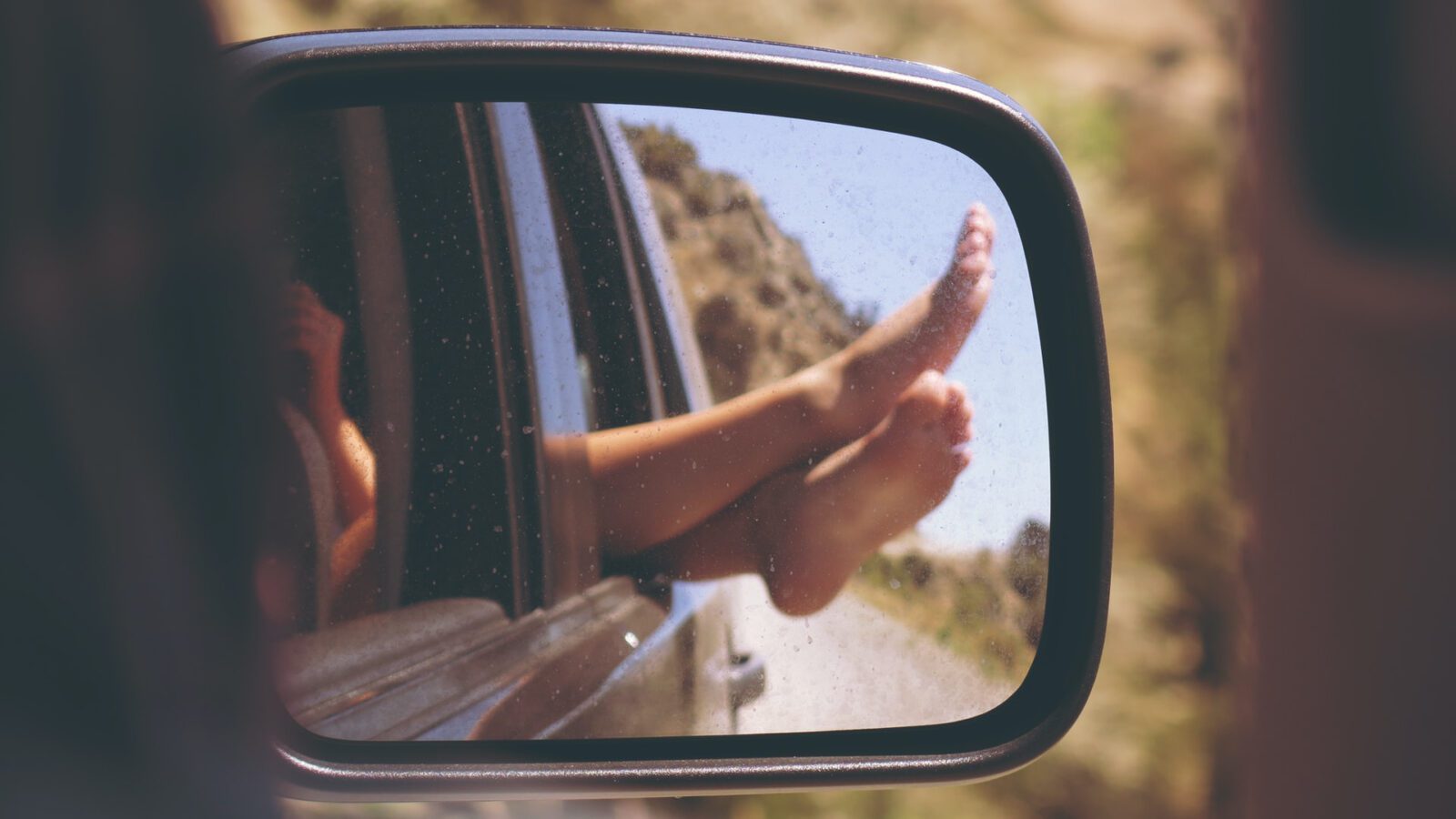 feet sticking out of car window, seen in side-view mirror